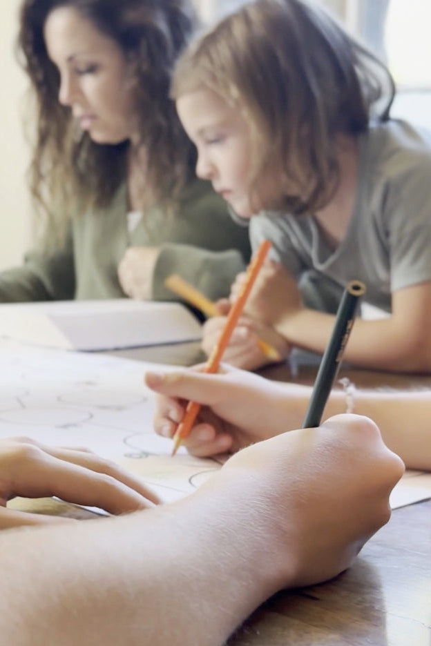 A group of children and adults sitting at a table, reading and writing in a book.